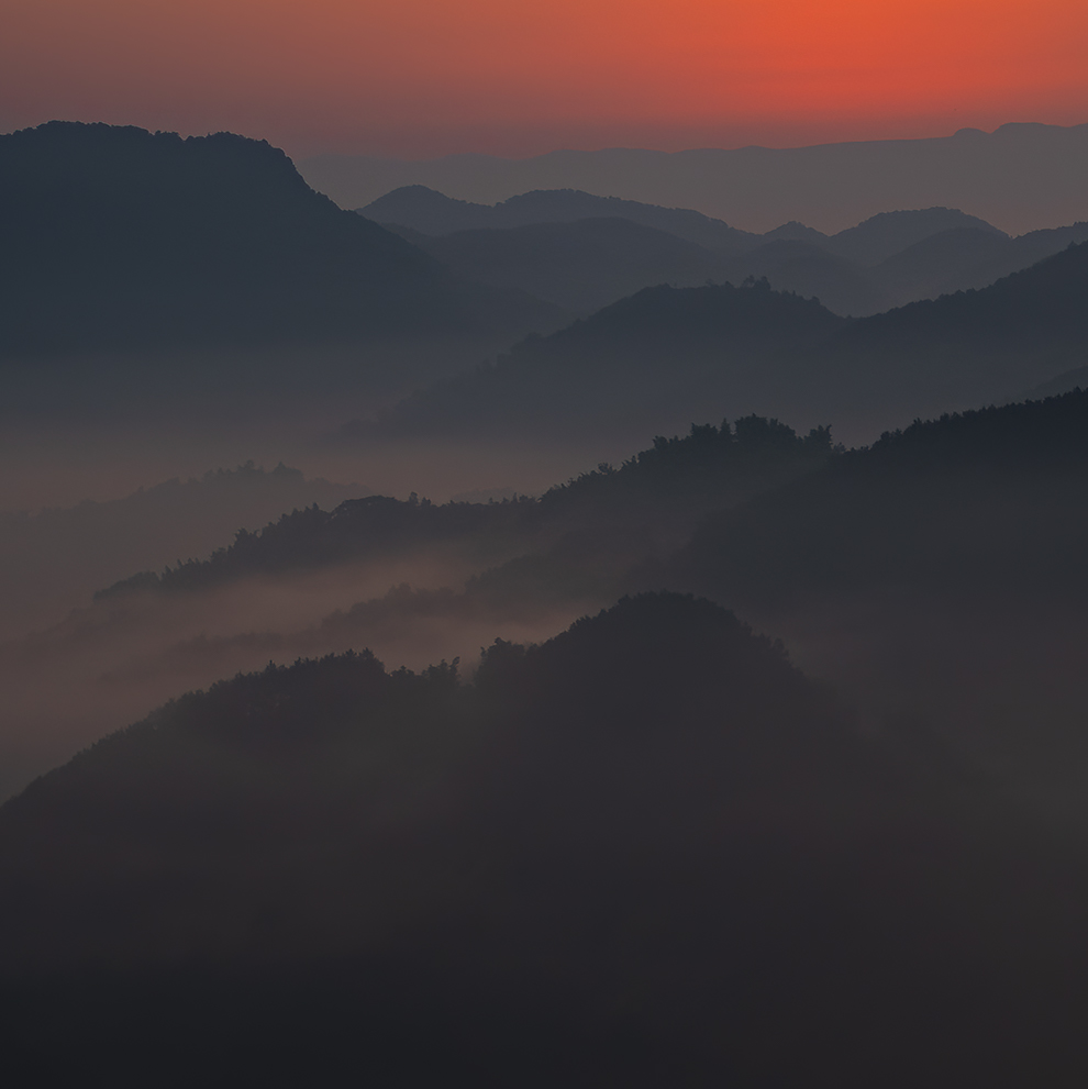 周家山日出时,近处深色山体与远处层叠的山脊形成对比,山谷雾气在山间淡淡散开。