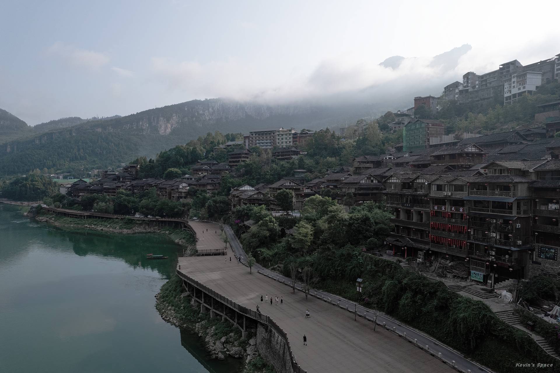 清晨云雾中的龚滩古镇与乌江,山坡建筑和滨水步道形成远近层次。